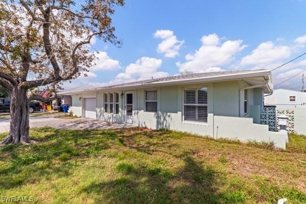 ranch-style home featuring concrete driveway, a front lawn, an attached garage, and stucco siding