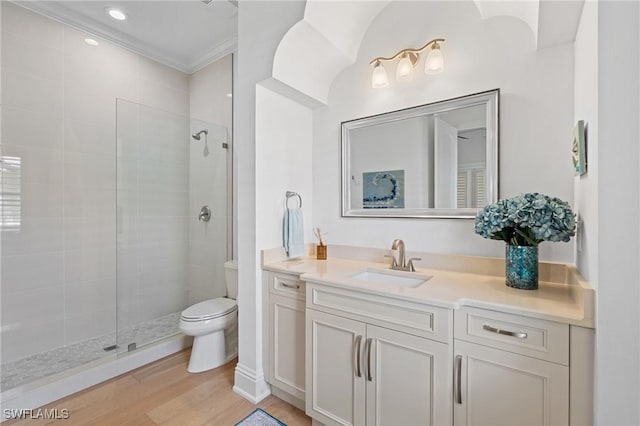 full bath with toilet, wood finished floors, vanity, tiled shower, and crown molding