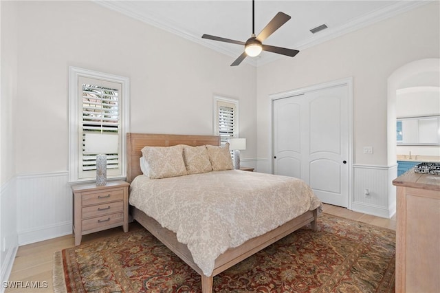 bedroom featuring light wood-style flooring, visible vents, ornamental molding, a closet, and wainscoting