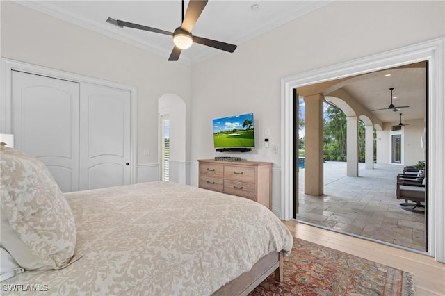 bedroom with access to exterior, arched walkways, a closet, ornamental molding, and wood finished floors