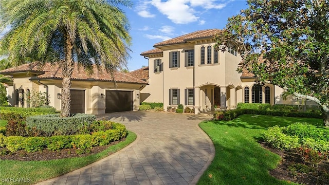 mediterranean / spanish-style house with a garage, a tiled roof, decorative driveway, a front lawn, and stucco siding