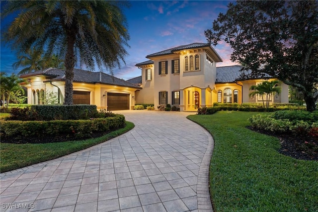 mediterranean / spanish-style house featuring decorative driveway, stucco siding, a lawn, a garage, and a tiled roof