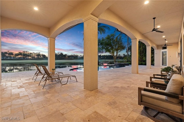 patio terrace at dusk featuring a water view and ceiling fan