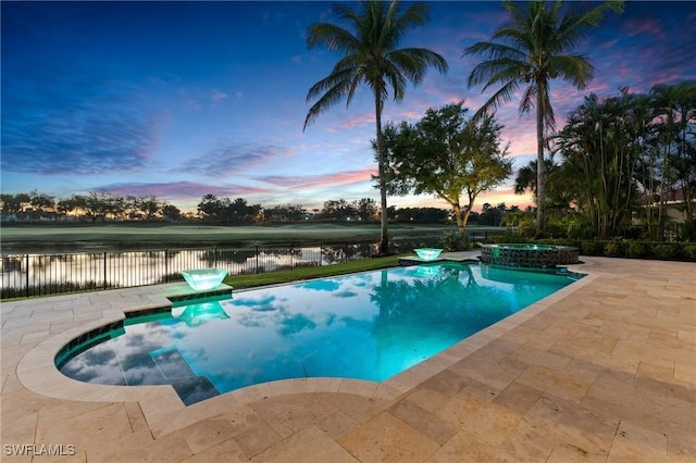 pool at dusk featuring a water view, a pool with connected hot tub, fence, and a patio