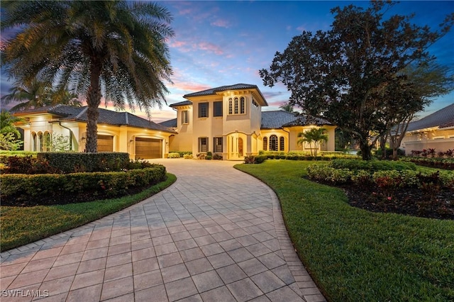 mediterranean / spanish house featuring a garage, a tile roof, decorative driveway, stucco siding, and a front lawn