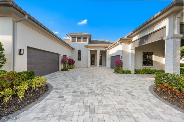 view of exterior entry featuring an attached garage, decorative driveway, and stucco siding