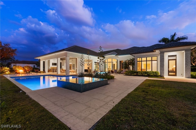 pool at dusk featuring a lawn, a patio area, and an outdoor pool