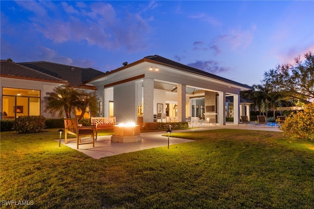 back of house at dusk featuring an outdoor fire pit, stucco siding, a patio, and a lawn