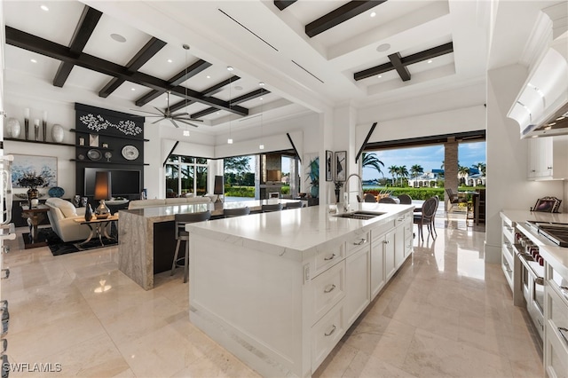 kitchen featuring a towering ceiling, a center island with sink, coffered ceiling, and a ceiling fan