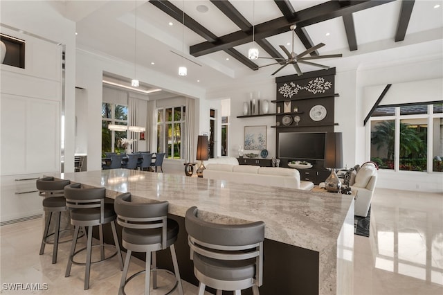 kitchen with light stone counters, pendant lighting, beamed ceiling, and a kitchen breakfast bar