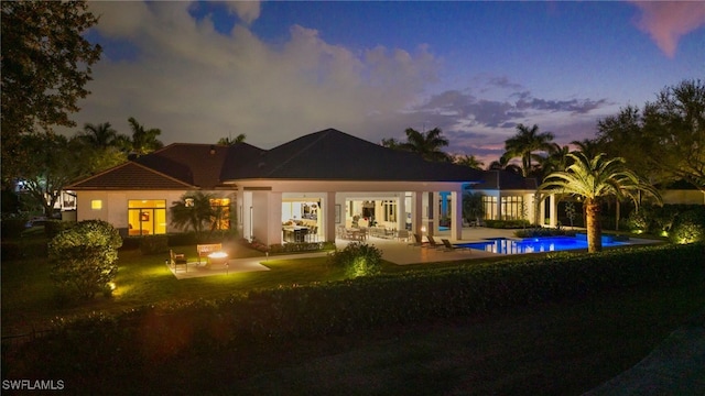 back of house at dusk featuring a yard, a patio area, and an outdoor pool