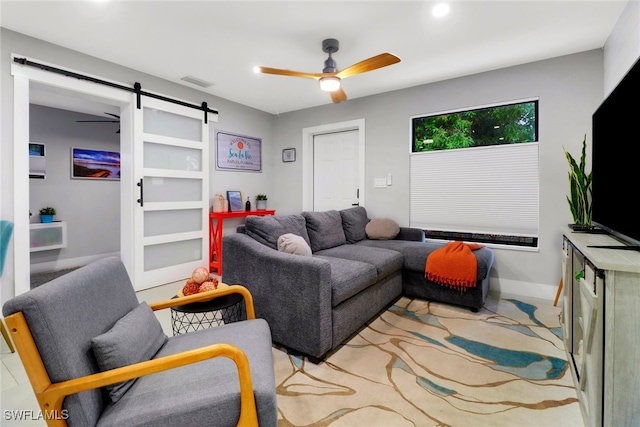 living area featuring ceiling fan, a barn door, visible vents, and baseboards