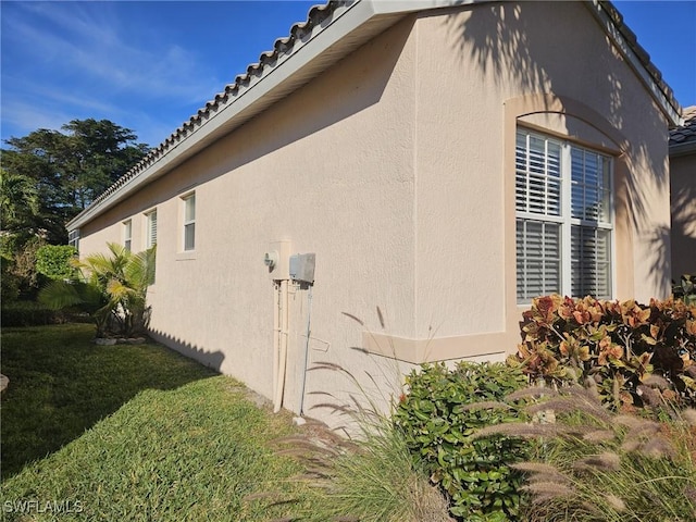 view of side of home featuring a tiled roof, a lawn, and stucco siding