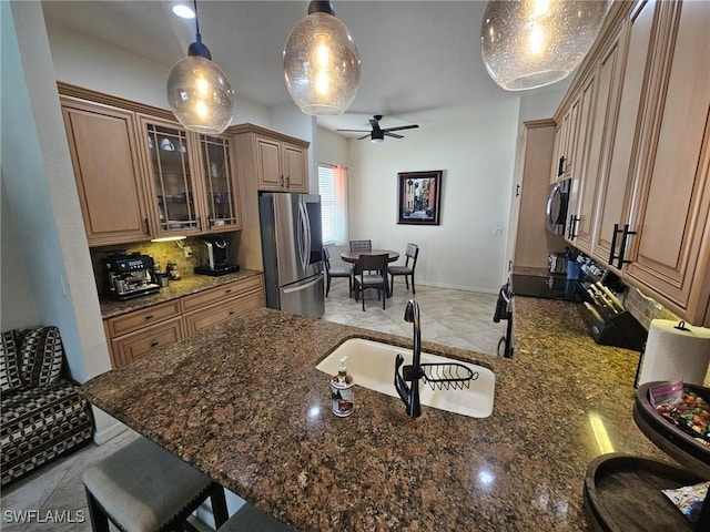 kitchen featuring a sink, a kitchen breakfast bar, appliances with stainless steel finishes, decorative backsplash, and dark stone counters