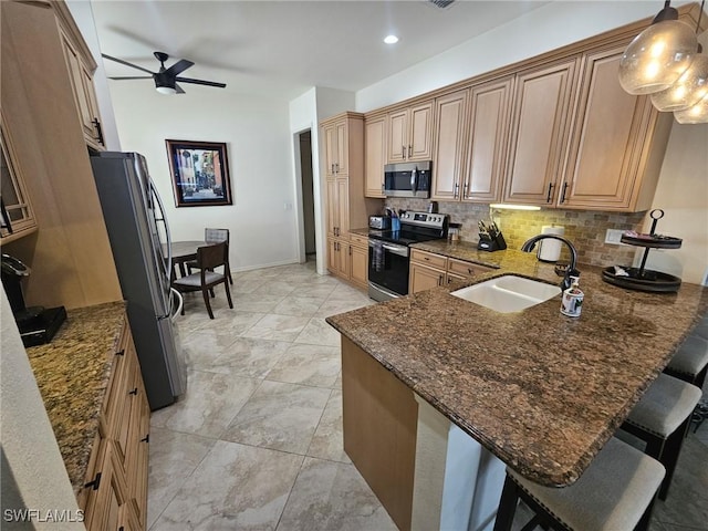 kitchen with stainless steel appliances, a peninsula, a sink, backsplash, and dark stone countertops