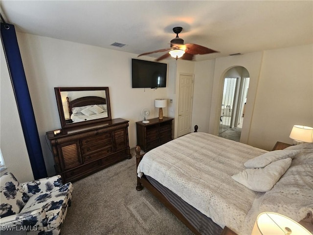 carpeted bedroom featuring ceiling fan, visible vents, and arched walkways