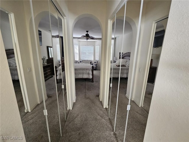 hallway with arched walkways, a textured wall, and carpet