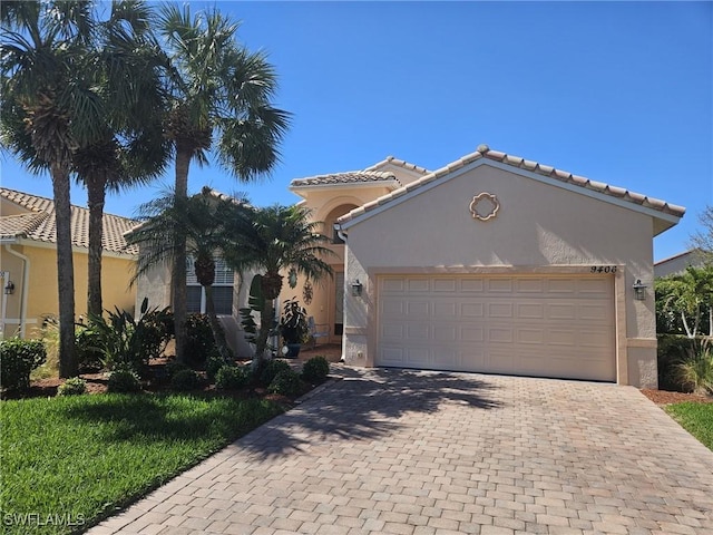 mediterranean / spanish-style house featuring a tiled roof, decorative driveway, an attached garage, and stucco siding