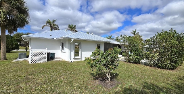 back of house with metal roof, a lawn, central AC unit, and stucco siding