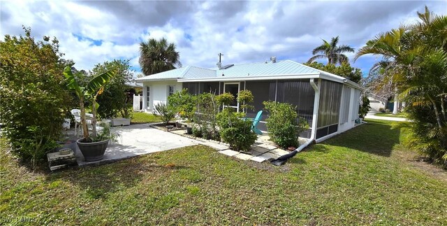 back of property with a sunroom, a patio area, metal roof, and a yard