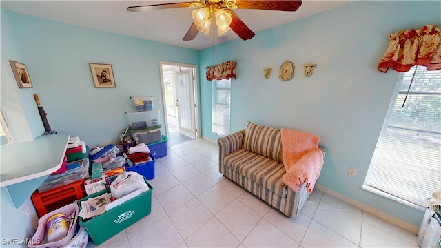 living area with light tile patterned floors, a ceiling fan, and baseboards