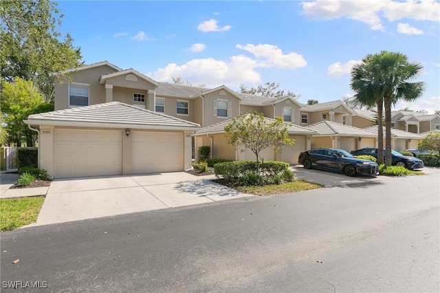 multi unit property with driveway, a garage, a tile roof, a residential view, and stucco siding