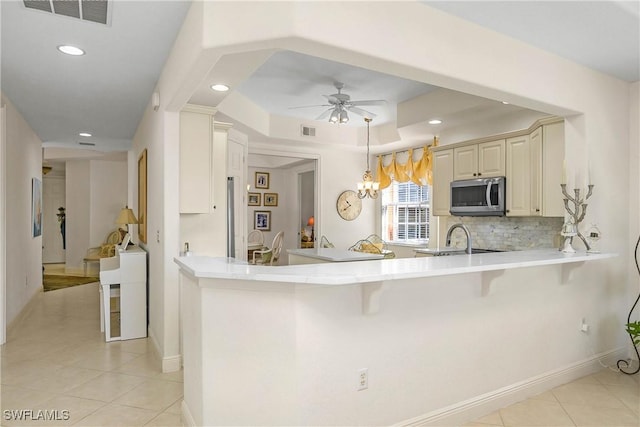 kitchen featuring light tile patterned flooring, a peninsula, visible vents, light countertops, and stainless steel microwave