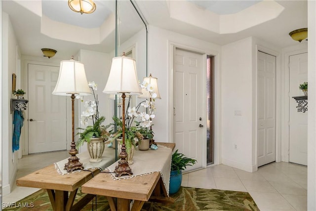 foyer entrance with light tile patterned floors, baseboards, and a tray ceiling