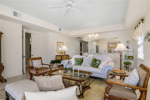 living room featuring ceiling fan with notable chandelier, a tray ceiling, and visible vents