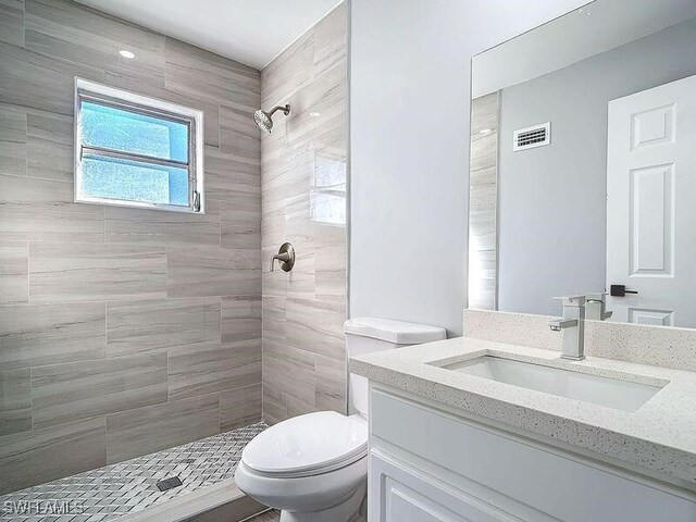 bathroom with toilet, tiled shower, and vanity