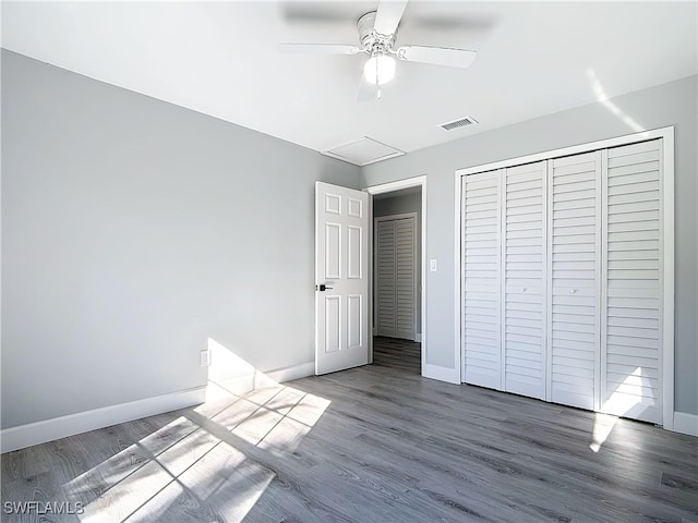 unfurnished bedroom with wood finished floors, a ceiling fan, baseboards, a closet, and attic access