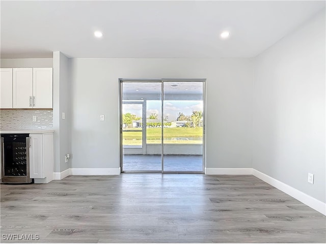 unfurnished living room featuring light wood finished floors, wine cooler, recessed lighting, and baseboards