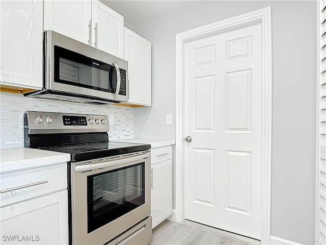 kitchen with light wood-style flooring, stainless steel appliances, white cabinets, light countertops, and tasteful backsplash