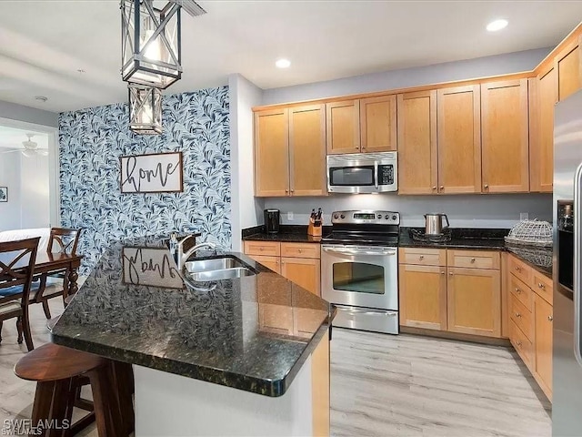 kitchen with recessed lighting, a sink, appliances with stainless steel finishes, light wood finished floors, and dark stone countertops