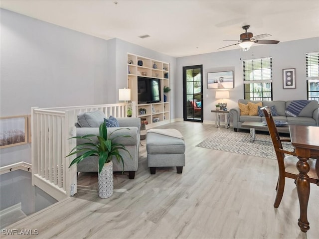 living room featuring a ceiling fan, visible vents, baseboards, and wood finished floors