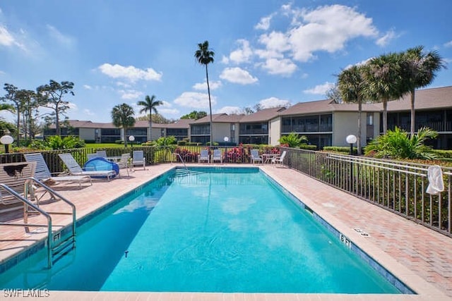 community pool with a patio area, fence, and a residential view