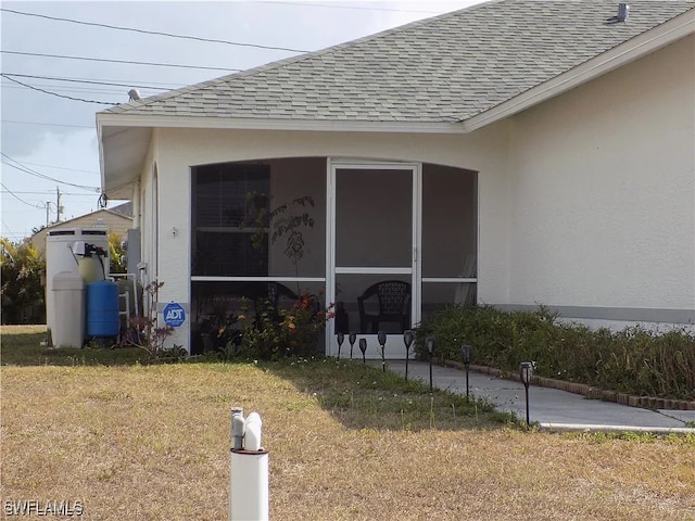 view of property exterior with a sunroom, roof with shingles, a lawn, and stucco siding