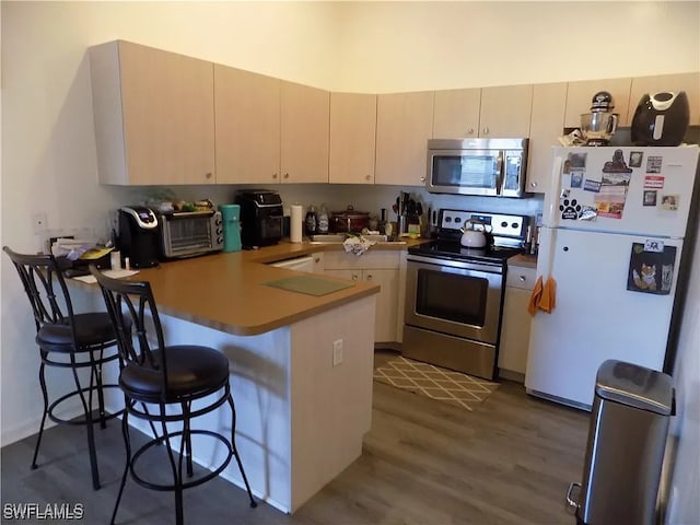 kitchen with appliances with stainless steel finishes, a breakfast bar, wood finished floors, a peninsula, and light countertops