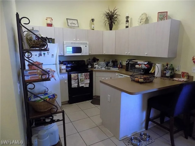 kitchen with light tile patterned floors, white cabinetry, white appliances, a peninsula, and a kitchen bar