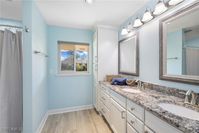 bathroom with double vanity, a sink, baseboards, and wood finished floors