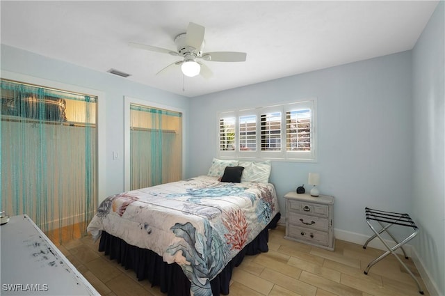 bedroom featuring light wood finished floors, multiple closets, visible vents, ceiling fan, and baseboards