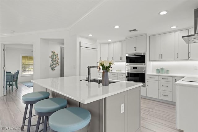 kitchen with visible vents, stainless steel double oven, a sink, paneled refrigerator, and a kitchen breakfast bar