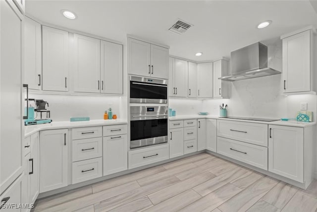 kitchen with stainless steel double oven, visible vents, white cabinets, light countertops, and wall chimney exhaust hood