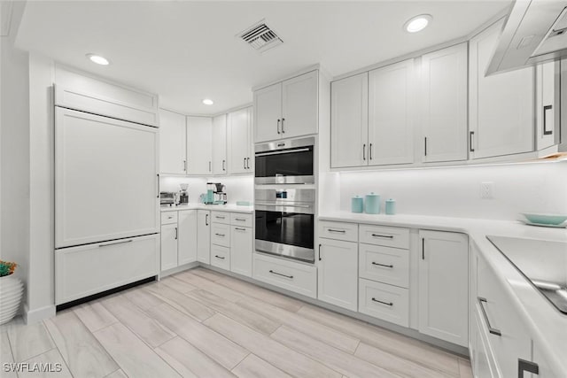 kitchen with stainless steel double oven, paneled built in refrigerator, visible vents, white cabinetry, and light countertops