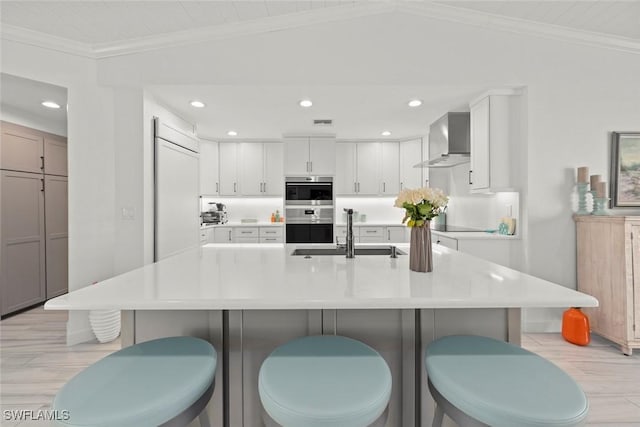 kitchen with wall chimney exhaust hood, ornamental molding, vaulted ceiling, double oven, and a sink