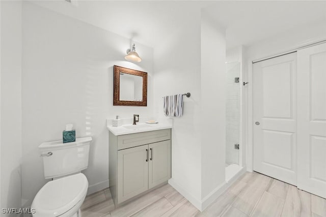 bathroom featuring wood finish floors, toilet, a stall shower, vanity, and baseboards