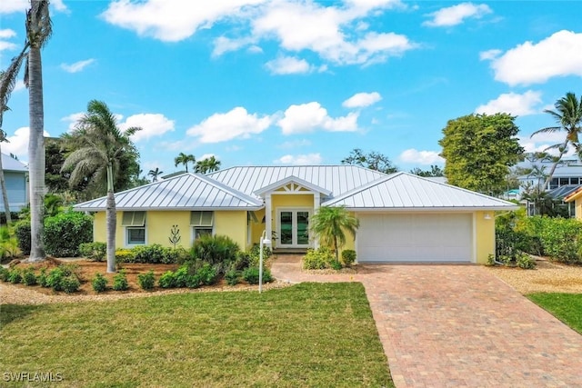 ranch-style home featuring decorative driveway, french doors, an attached garage, a front yard, and a standing seam roof