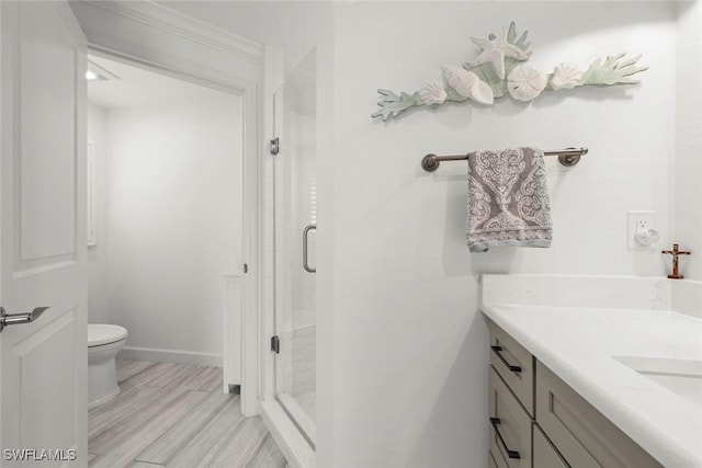 bathroom with toilet, a stall shower, vanity, wood finished floors, and baseboards