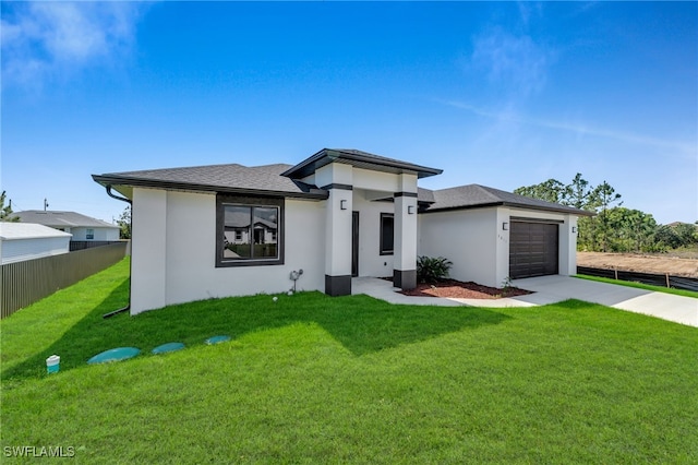 prairie-style house featuring an attached garage, fence, concrete driveway, stucco siding, and a front yard