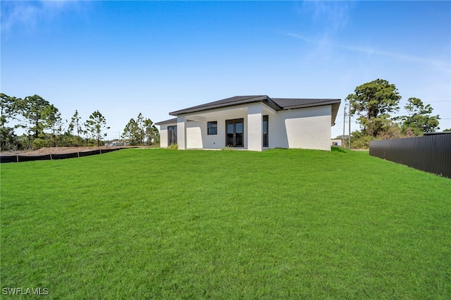 rear view of property with stucco siding, a yard, and fence